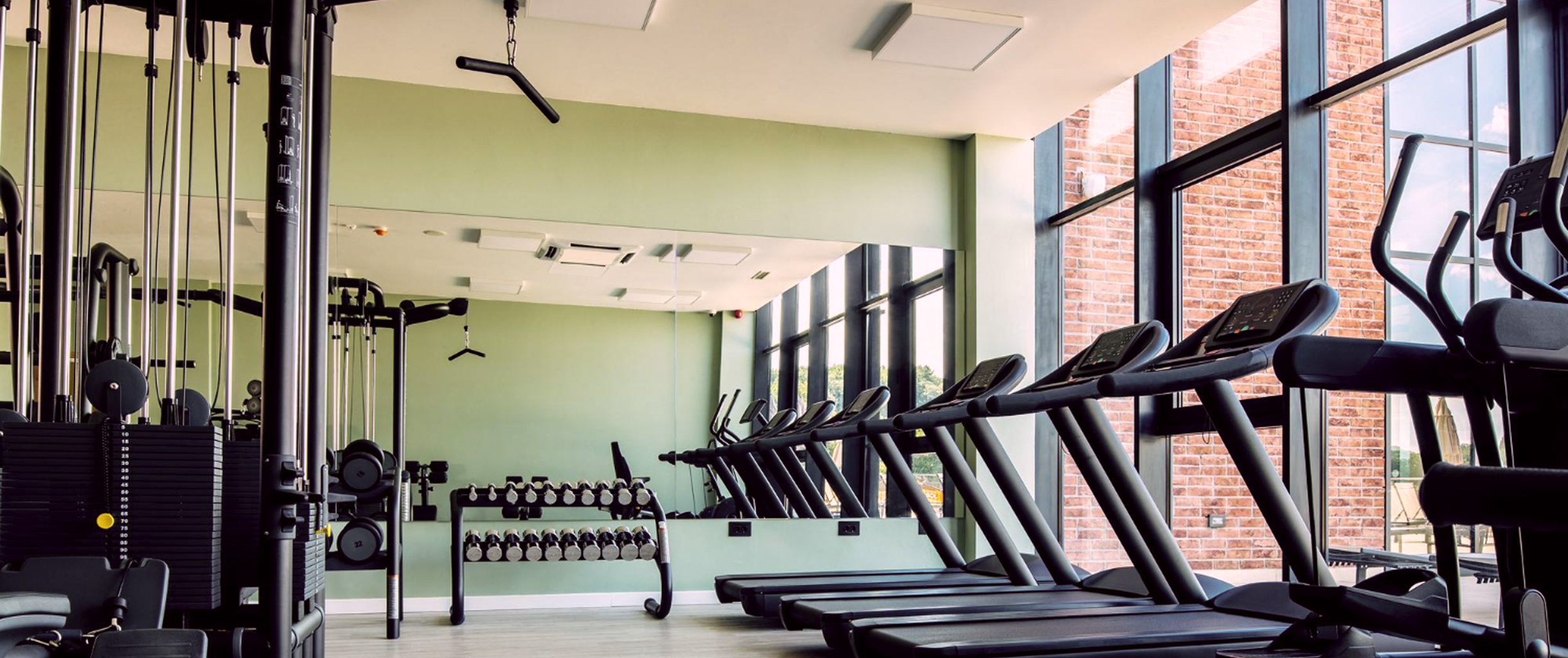 Комната с панорамными окнами, а в ней рядом с окнами беговые дорожки, рядом стоят другие тренажеры